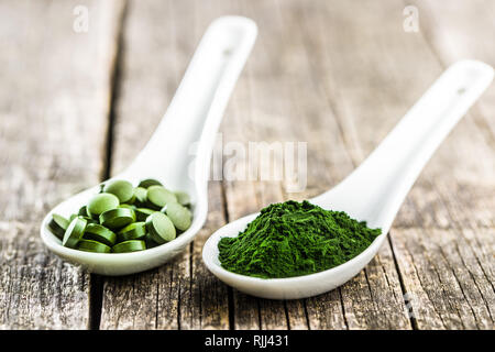 La chlorelle vert comprimés ou l'orge en pilules et en poudre dans une cuillère en céramique. Banque D'Images