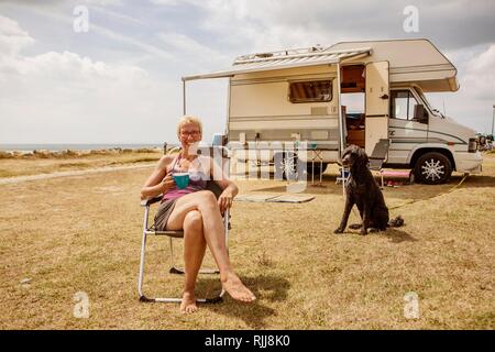 Femme assise avec un chien, caniche, King en face de son camping car et de boire du café pendant les vacances au bord de la mer, Houlgate, Normandie Banque D'Images