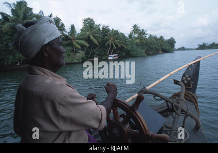 Le capitaine d'une péniche guide son navire à travers la myriade de backwater du Kerala. Banque D'Images