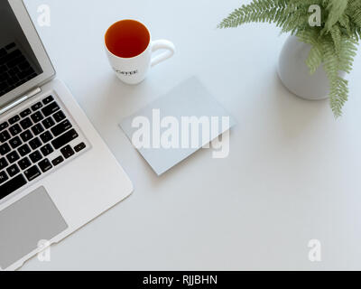 Vue de dessus d'un bureau à domicile bureau, avec un ordinateur portable, d'une tasse de café, une plante et une photo. Banque D'Images