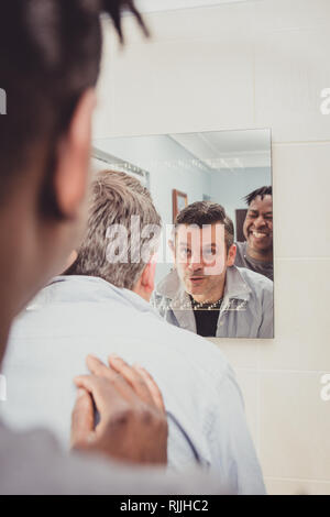 Un couple gay ensemble en face de la salle de bains miroir. Banque D'Images