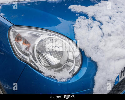 Capot de voiture avec la fonte de la neige et des projecteurs exposés. Banque D'Images