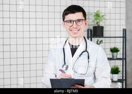 Happy smiling young doctor writing on clipboard dans un hôpital moderne Banque D'Images