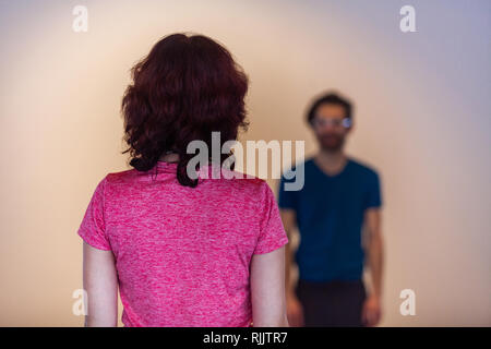 Femme debout loin devant un homme. Femme vu de dos, debout devant un homme flou en arrière-plan avec une certaine distance entre eux. Banque D'Images