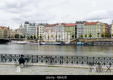 Jeune homme assis le long des rives de la rivière Vltava, en face de la maison qui danse, Prague, République Tchèque Banque D'Images