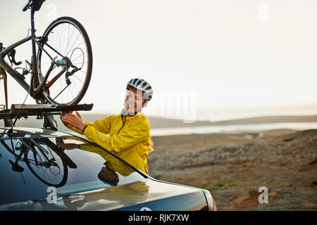 Souriante jeune femme attacher son vélo sur le toit de sa voiture. Banque D'Images