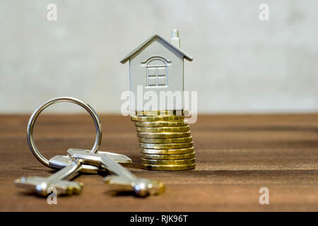 Le symbole de la maison de gris sur une pile de pièces jaune brillant avec deux touches de métal sur un fond de bois brun combiné et a lavé hors de l'conc Banque D'Images