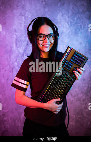 Belle Friendly Gamer Girl Posing de banderoles avec un clavier dans les mains, portant des lunettes. Jolie fille Geek avec néon couleurs rétro Cool dans Banque D'Images