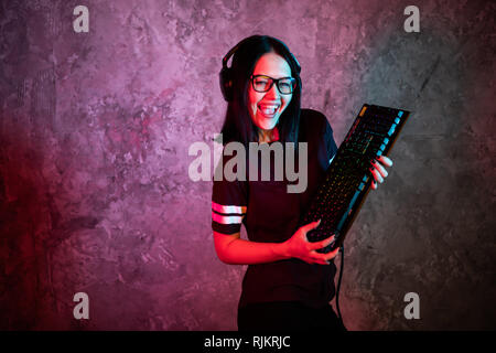 Belle Friendly Gamer Girl Posing de banderoles avec un clavier dans les mains, portant des lunettes. Jolie fille Geek avec néon couleurs rétro Cool dans Banque D'Images