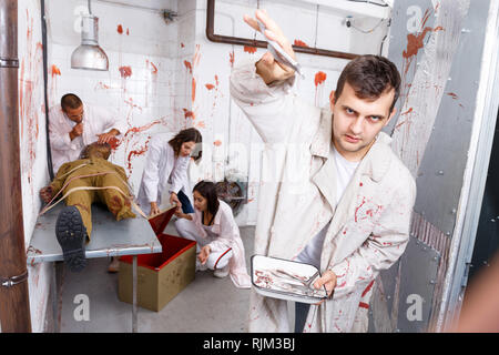 Guy s'amusant avec des amis en quête prix en chambre chirurgicale avec des traces de sang, effrayant avec des instruments médicaux sur l'appareil photo Banque D'Images