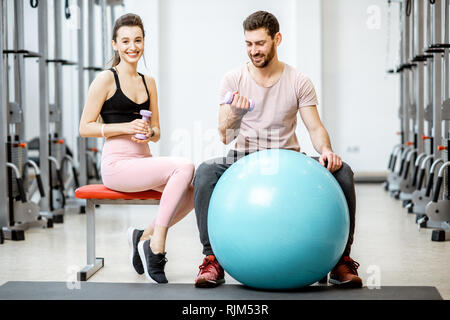 Portrait of a young couple sitting avec fitness ball pendant la pause à la salle de sport de réadaptation Banque D'Images