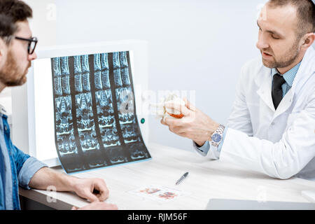 L'homme au cours de la consultation médicale avec thérapeute principal à la recherche sur le modèle de vertèbres au bureau Banque D'Images