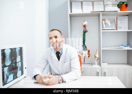 Portrait d'un thérapeute principal assis avec x-ray modèles anatomiques et d'impression au bureau Banque D'Images