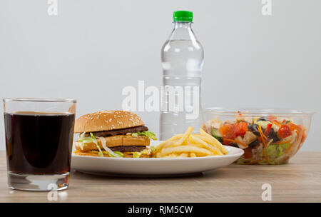 Double cheeseburger avec des frites de pommes de terre et du coke vs poulet sain et légumes salade et encore de l'eau. lequel choisir ? Banque D'Images