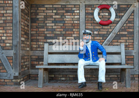 Un marin avec tuyau et est assis sur un banc en face d'un mur de pierre Banque D'Images