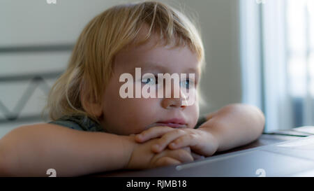 Une belle photo d'un adorable garçon s'appuyant sur ses mains sur une table et à la recherche à la distance. Banque D'Images