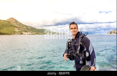 Young handsome man smiling plongeur prêt à plonger dans l'eau froide combinaison, palmes, ceinture de plomb et de oxigen à Karaburun, Izmir. La Turquie Banque D'Images