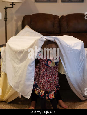 Deux Caucasian girl enfants jouant avec tente de fortune faite à partir d'une feuille à l'intérieur meubles drapée sur. Banque D'Images