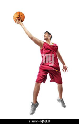 Joueur de basket-ball homme asiatique attrayant en uniforme rouge sautant avec balle en mains isolé sur fond blanc Banque D'Images