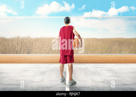 Vue arrière du joueur de basket-ball asiatique homme debout avec balle sur sa main dans la piscine en plein air de basket-ball Banque D'Images