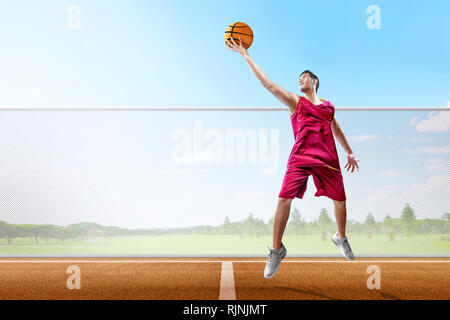 Joueur de basket-ball homme asiatique excité avec ballon en main sautant haut sur le terrain de basket-ball Banque D'Images