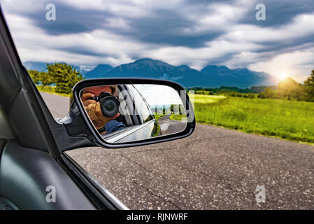 Réflexion d'un photographe avec un appareil photo dans le rétroviseur d'une voiture dans la nature. Banque D'Images