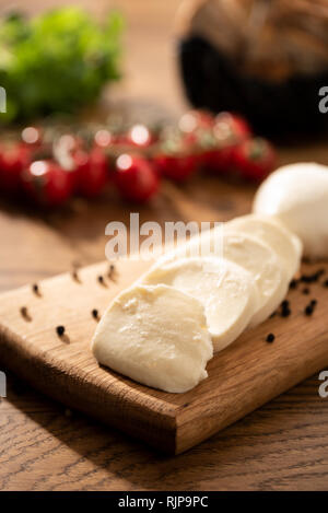 Le mozzarella sur planche en bois. Tomates cerises en arrière-plan. Table en bois avec la composition des aliments italiens Banque D'Images