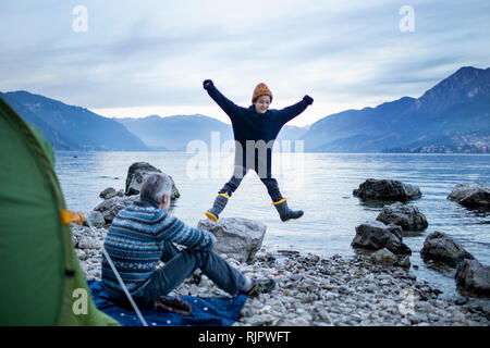 Père Fils faisant regarder star jump par Lakeside, Onno, Lombardie, Italie Banque D'Images