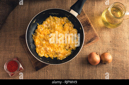 Photo des œufs brouillés avec du paprika, d'oignons et d'huile d'en haut - style rural. Le jaune des oeufs brouillés en noir sur fond de jute pan. Banque D'Images