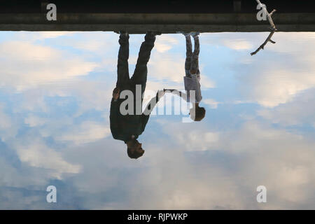 Reflet de père et fille se tenant la main sur un quai dans l'eau au milieu de beaux nuages Banque D'Images