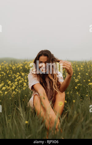 Jeune femme assise dans le champ de fleurs sauvages jaunes, portrait, Californie, Etats-Unis, Jalama Banque D'Images