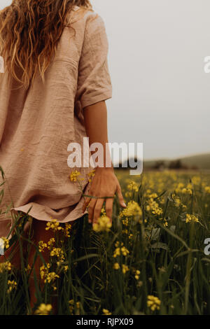 Jeune femme marche dans le champ de fleurs sauvages jaunes, vue arrière, Jalama, California, USA Banque D'Images