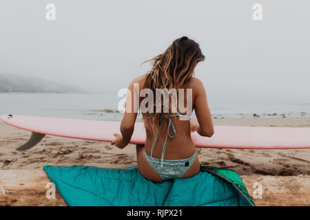 Jeune femme surfer assis sur se connecter à à surfboard on beach, vue arrière, Ventura, Californie, USA Banque D'Images