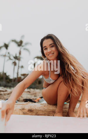 Jeune femme assise sur surfer journal à plage, portrait, Ventura, Californie, USA Banque D'Images