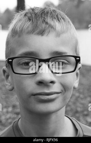 Portrait noir et blanc d'un garçon caucasien preteen avec des lunettes et un petit sourire narquois Banque D'Images