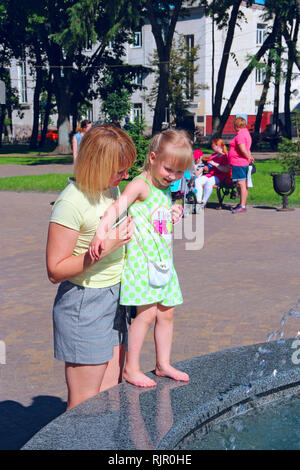 Mère et sa fille jouant près des fontaines de la ville en parc. Mère de sa fille, laver les pieds en fontaines. Circuit de refroidissement par temps chaud. Drôle de week-end Banque D'Images