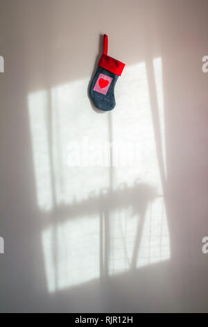 Chaussette de Noël rouge avec un coeur accroché sur mur blanc avec l'ombre d'une fenêtre Banque D'Images