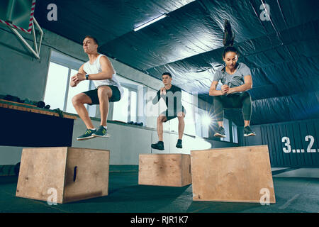 Groupe de personnes sont au travail musculaire sportive au gymnase. Mettre en place la formation. Sautant sur un fort ensemble. Les hommes et les femmes à un club de santé. Concept de vie sain Banque D'Images