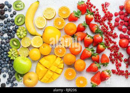 Arc-en-ciel colorés baies fruits sur fond blanc. Vue de dessus de bleuets fraises mangue cerises citrons oranges pommes groseilles prunes Banque D'Images