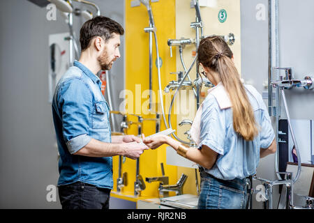 Jeune couple choisir robinet de douche debout près de la belle vitrine de l'atelier de plomberie Banque D'Images