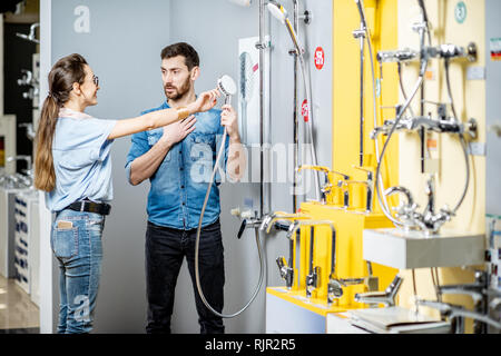 Jeune couple choisir robinet de douche debout près de la belle vitrine de l'atelier de plomberie Banque D'Images