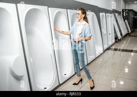 Jeune femme de choisir de nouveaux meubles de salle de bain, debout près de la vitrine avec une baignoire en acrylique blanc supermarché dans l'immeuble Banque D'Images