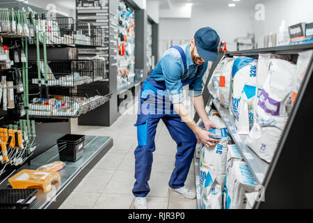 Workman en salopette bleue en tenant un sac avec mélange de construction, l'achat de matériaux pour la réparation dans l'immeuble supermarché Banque D'Images