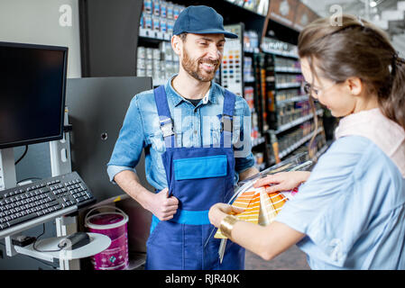 Jeune femme choisir client la peinture de couleurs du nuancier, debout avec workman en supermarché avec produits de construction Banque D'Images
