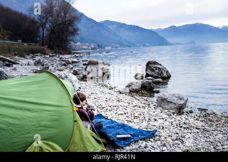 Garçon assis sur une couverture devant tente de boire du café au bord du lac, sur le lac de Côme, Onno, Lombardie, Italie Banque D'Images