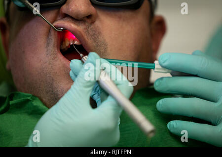 Les détails avec les mains d'une femme dentiste, avec des gants chirurgicaux, le travail avec les instruments au laser à l'intérieur de la bouche d'un patient Banque D'Images