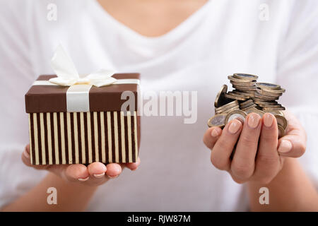 Close-up of Woman's Hand Holding Gift Box avec ruban blanc et pile de pièces Banque D'Images