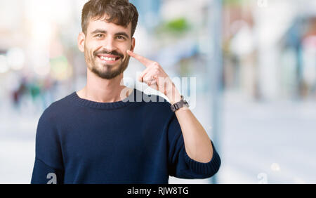 Jeune homme séduisant sur fond isolé pointant du doigt à la main sur le visage et le nez, sourire joyeux Banque D'Images