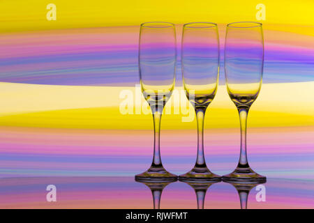 Trois verres de champagne dans une rangée avec un arc-en-ciel de couleurs de peinture de lumière derrière eux Banque D'Images