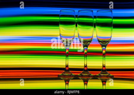 Trois verres de champagne dans une rangée avec un arc-en-ciel de couleurs de peinture de lumière derrière eux Banque D'Images